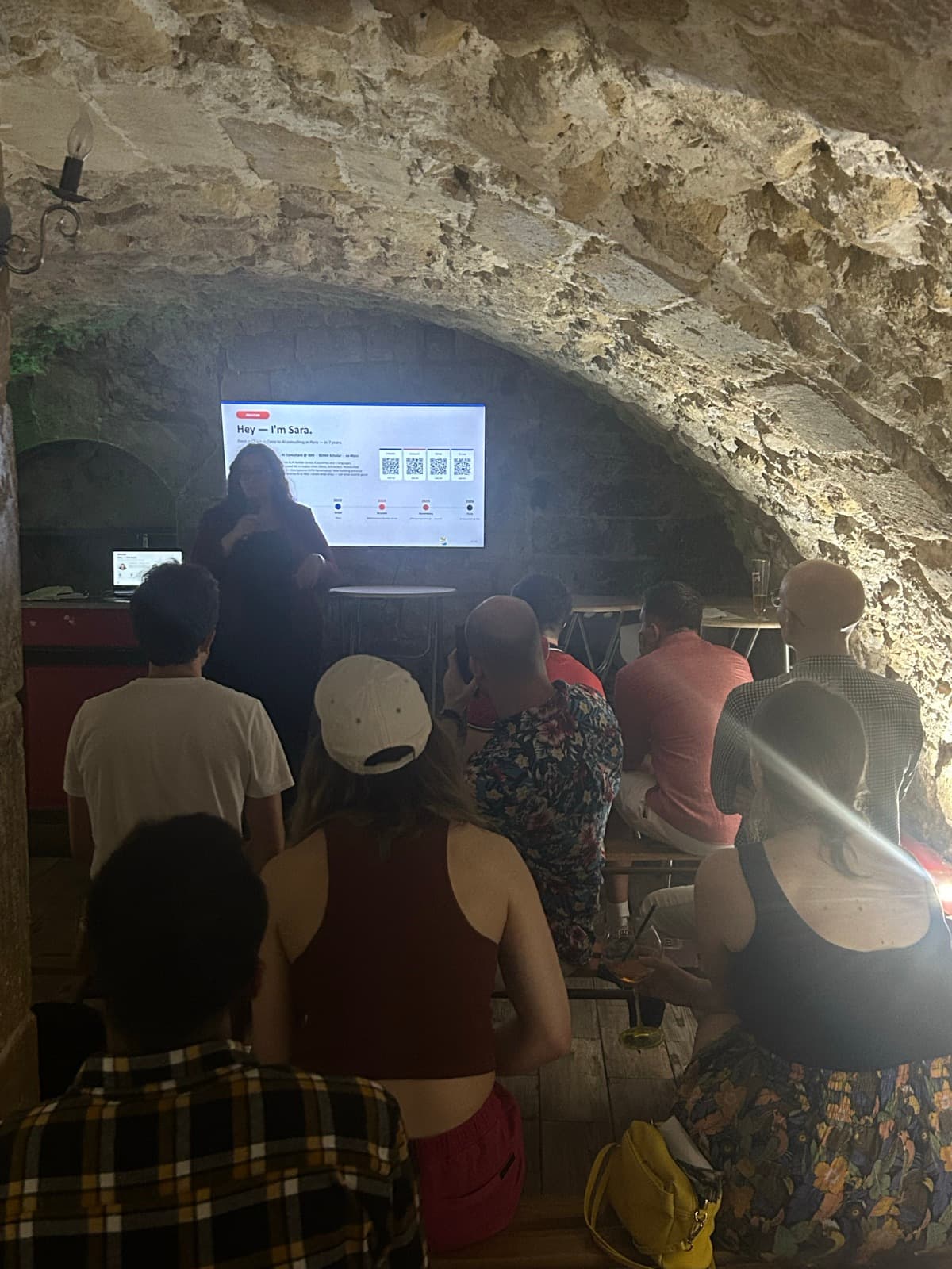 A speaker presenting to the crowd at an AI Builders Night in a stone-vaulted Paris venue